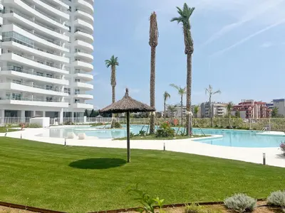 a resort with a pool and palm trees and a building at Global Vacacional, Apartamento de 2 habitaciones con gran terraza en Gran Canet in Canet de Berenguer