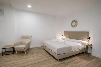 a white bedroom with a bed and a chair at Cid Flats by Concept in Valencia