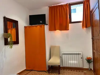 a room with orange curtains and a chair and a television at Casa rural La Boticaria in Villar del Arzobispo