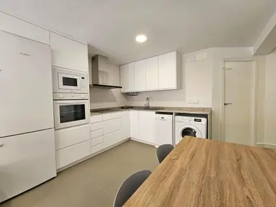 a kitchen with white cabinets and a wooden table at Apartamento a pie de playa I in Faro de Cullera