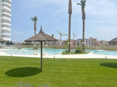 a resort with a pool and a umbrella in the grass at Global Vacacional, Moderno apartamento con terraza en Gran Canet in Canet de Berenguer