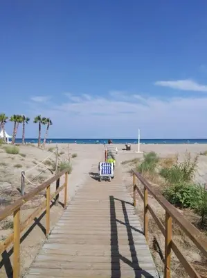 a person sitting on a bench on a boardwalk at the beach at Luminoso piso en edificio de canet de berenguer in Canet de Berenguer