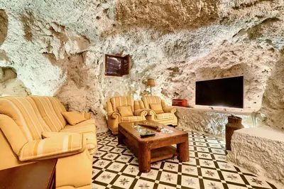 a living room with couches and a tv in a rock wall at Cueva con jacuzzi a 20 minutos de Valencia in Benaguacil