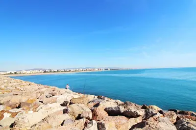 a person sitting on a rocky shoreline with the ocean at Global Vacacional, Practico apartamento para 6 personas en Puerto Sagunto in Puerto de Sagunto