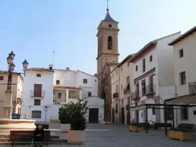 a woman sitting on a bench in a street with a church at Apartamentos Bobal Requena in Requena
