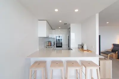 a kitchen with a white counter and wooden stools at Global Vacacional, Apartamento con vistas al mar, 2 terrazas y piscina en Canet d'en Berenguer in Canet de Berenguer