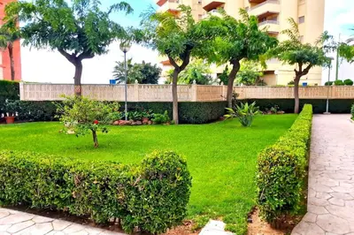 a green yard with trees and a building at Bonito apartamento con vistas al mar in Playa Pobla de Farnals