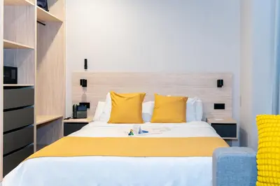a bedroom with a bed with yellow pillows and a chair at Dorm4You Arena 2 in Valencia