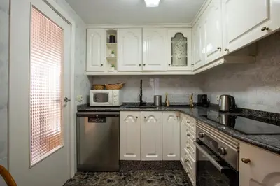 a kitchen with white cabinets and a stainless steel refrigerator at Apartamento en complejo residencial con piscina y garaje a 100m del mar in Las Canteras