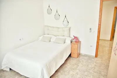 a white bedroom with a white bed and a wooden nightstand at Apartamento Playa Xilxes in Xilxes