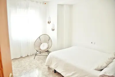 a bedroom with a bed and a chair next to a window at Apartamento Playa Xilxes in Xilxes
