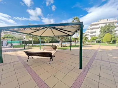 a park with two benches under a large umbrella at Global Vacacional, Práctico apartamento en la playa de Canet in Canet de Berenguer