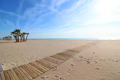 a beach with footprints in the sand and palm trees at Global Vacacional, Práctico apartamento en la playa de Canet in Canet de Berenguer