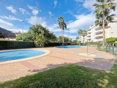a swimming pool with palm trees and a building at Global Vacacional, Práctico apartamento en la playa de Canet in Canet de Berenguer