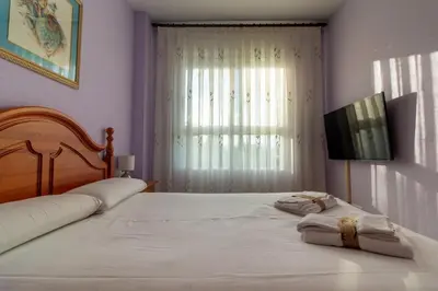 a bedroom with two beds and a television and a window at Global Vacacional, Piso práctico, con terraza y piscina en la playa de Canet in Canet de Berenguer