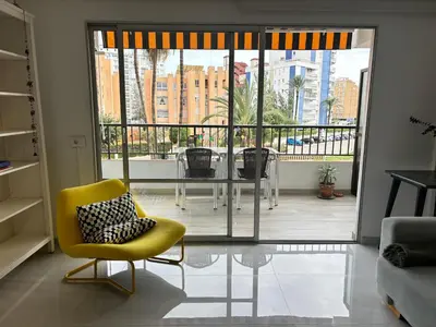 a living room with a yellow chair and a balcony at Apt. En la Playa, Wifi rápido y piscina. in Puebla de Farnals