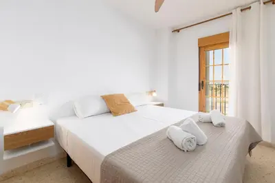 a white bedroom with two beds and a window at Travel Habitat Port Saplaya con vistas al Mar in Port Saplaya