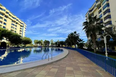 a swimming pool with palm trees and buildings at Apto con vistas a la playa de La Patacona in Valencia
