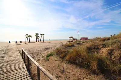 a beach with palm trees and a wooden boardwalk at Global Vacacional, Planta Baja con Piscina en Canet de Berenguer in Canet de Berenguer