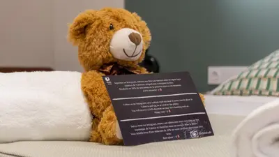 a brown teddy bear sitting on a bed with a sign at Osito Hub - Pintor Nicolau in Valencia