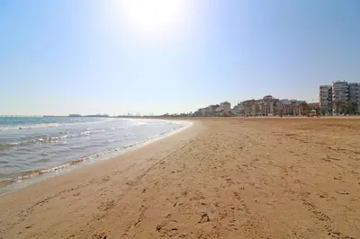 a sandy beach with buildings and the ocean at Global Vacacional, Apartamento cerca de la playa en Puerto Sagunto in Puerto de Sagunto