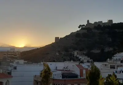 a view of a city with the sun setting on a hill at Ático Playa Cullera in Cullera