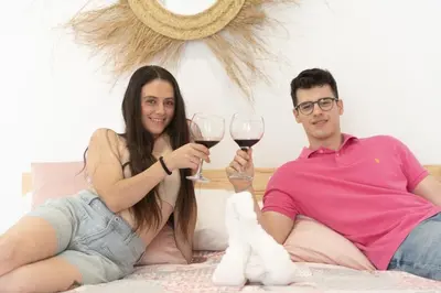 a man and woman sitting on a bed holding wine glasses at ALZIRA BONiTA SUITE ViP jacuzzi in Alzira