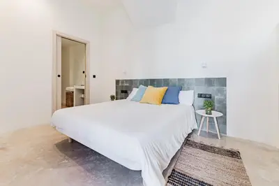 a white bedroom with a large bed with blue and yellow pillows at Loft Viñas in Valencia