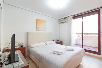 a white bedroom with a bed and a television at Global Vacacional, Apartamento muy cerca de la playa de Puerto de Sagunto in Puerto de Sagunto