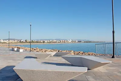 a row of benches next to a body of water at Global Vacacional, Apartamento muy cerca de la playa de Puerto de Sagunto in Puerto de Sagunto