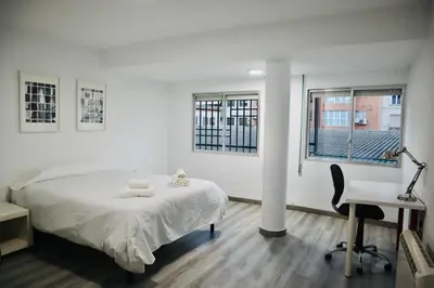 a white bedroom with a bed and a desk and two windows at Big Flat Ruzafa in Valencia