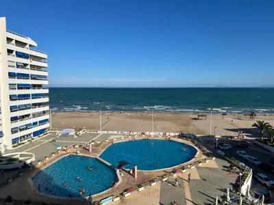 a large swimming pool next to a beach with a building at El Prado - Primera Línea Playa Cullera in Valencia