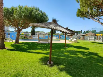 a grass umbrella in a park with a pool at Global Vacacional, Apartamento de 3 habitaciones en urbanización cerca del mar in Canet de Berenguer