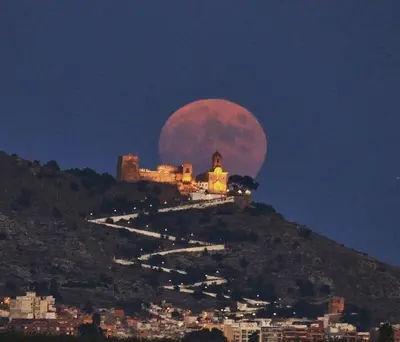a blood moon rising over a hill with a city at Villa conectada al mediterraneo, Infinity pool in Faro de Cullera