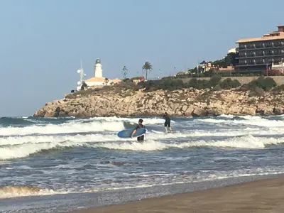 two people riding the waves on surfboards in the ocean at La Calita del Versalles in Faro de Cullera
