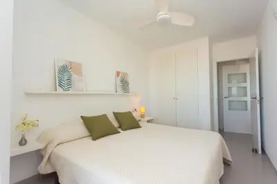 a white bedroom with a white bed with green pillows at Beachfront apartment Cullera Espacio in Cullera
