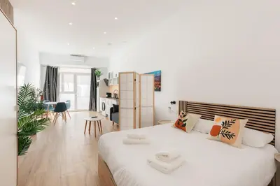 a white bedroom with a large bed and a kitchen at Stylish Studio with Easy Access to Valencias Best in Valencia
