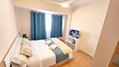 a bedroom with a bed with blue curtains and a television at Sagunto Beach Apartment 500m to Sea, WiFi 600Mb y AC in Puerto de Sagunto
