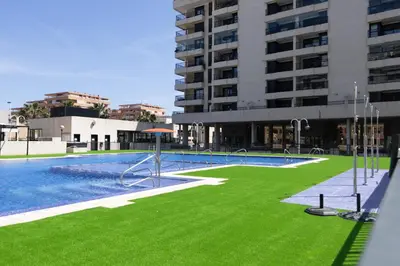 a swimming pool with green grass in front of a building at Apartamento con Vistas al mar, Piscina y Pista de Paddle in Valencia