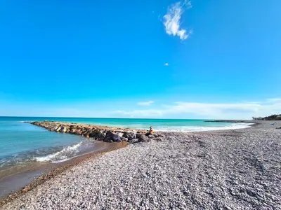 a person sitting on a rocky beach next to the ocean at Apartamento con Terraza junto al Mar en Moncofa in Moncófar