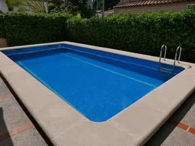 a blue swimming pool in front of a hedge at Natural park, terrace and pool in Partida de La Cañada