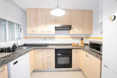 a kitchen with wooden cabinets and a black appliance at Dúplex tranquilo frente al mar en Xilxes Terraza, parking y WiFi in Chilches