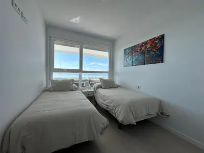two beds in a white room with a window at Gran Canet Salva, moderno apartamento con terraza y vistas al mar in Canet de Berenguer