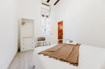 a white bedroom with a bed and a chair at Hogar con encanto a 10 min del centro de Valencia in Valencia