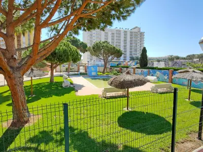 a fence in a park with chairs and an umbrella at Global Vacacional, apartamento de una habitación en urbanización con piscina in Canet de Berenguer