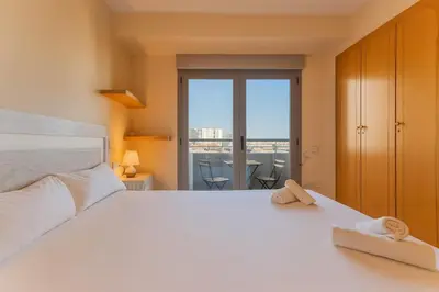 a bedroom with a large white bed with a balcony at Tu refugio moderno en Valencia - piscina, gimnasio y padel incluidos in Valencia