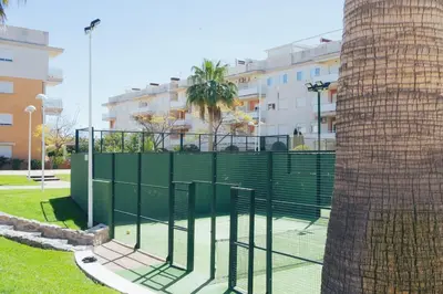 a tennis court with a fence next to a tree at Blanca Mar in Barrio-Mar
