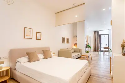 a white bedroom with a bed and a living room at Hridaya El Grao close to the sea in Valencia