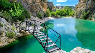 a metal bridge over a river with green water at Casa de Madera I - Naturaleza y Experiencias in Bicorp