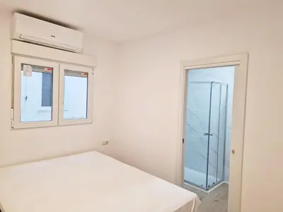 a white bedroom with a bed and a window at Cabanyal playa las arenas apartamento reformado in Valencia